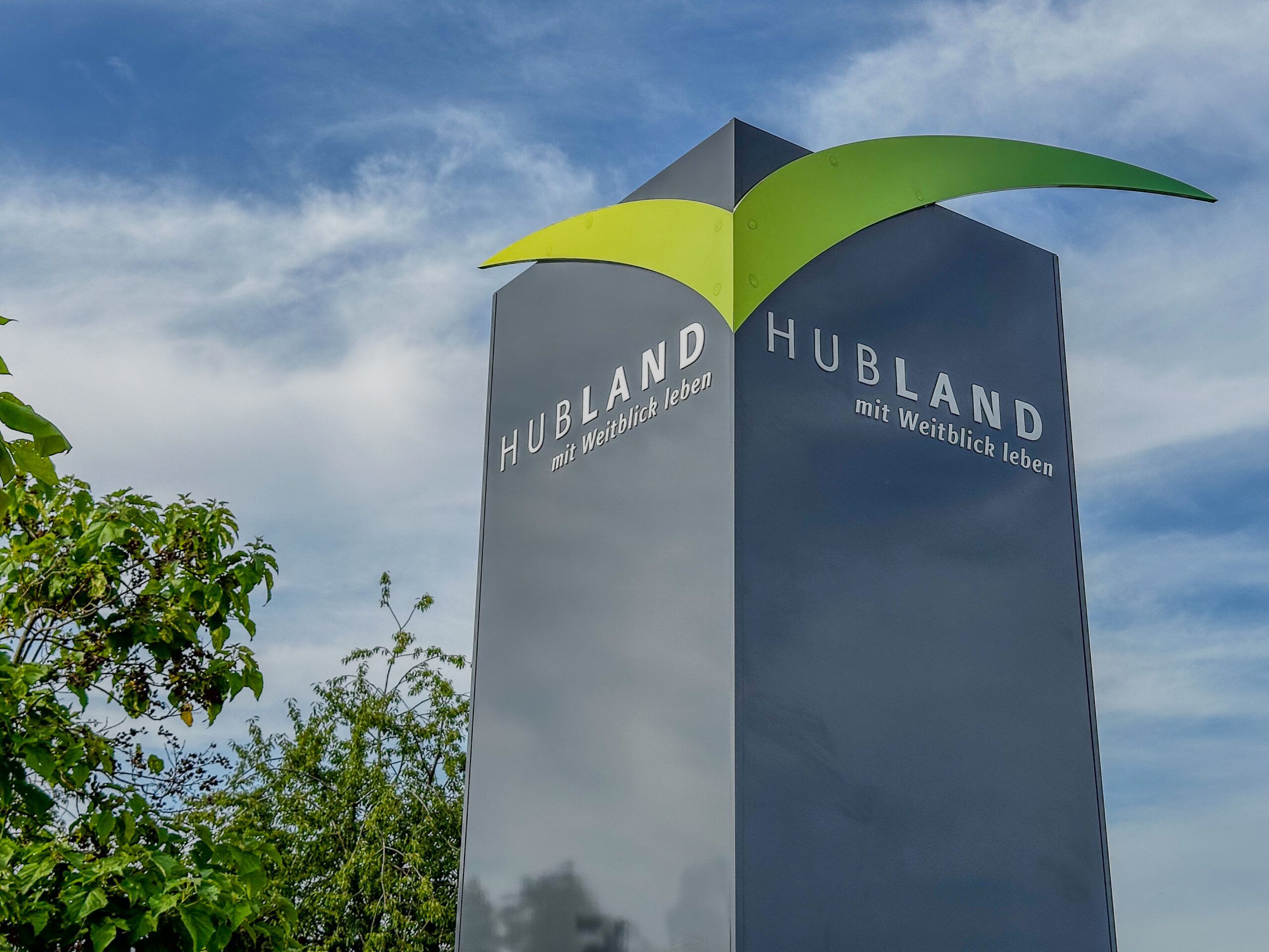 Großes graues Schild im Stadtteil Hubland in Würzburg mit dem Slogan 'Hubland mit Weitblick leben'.