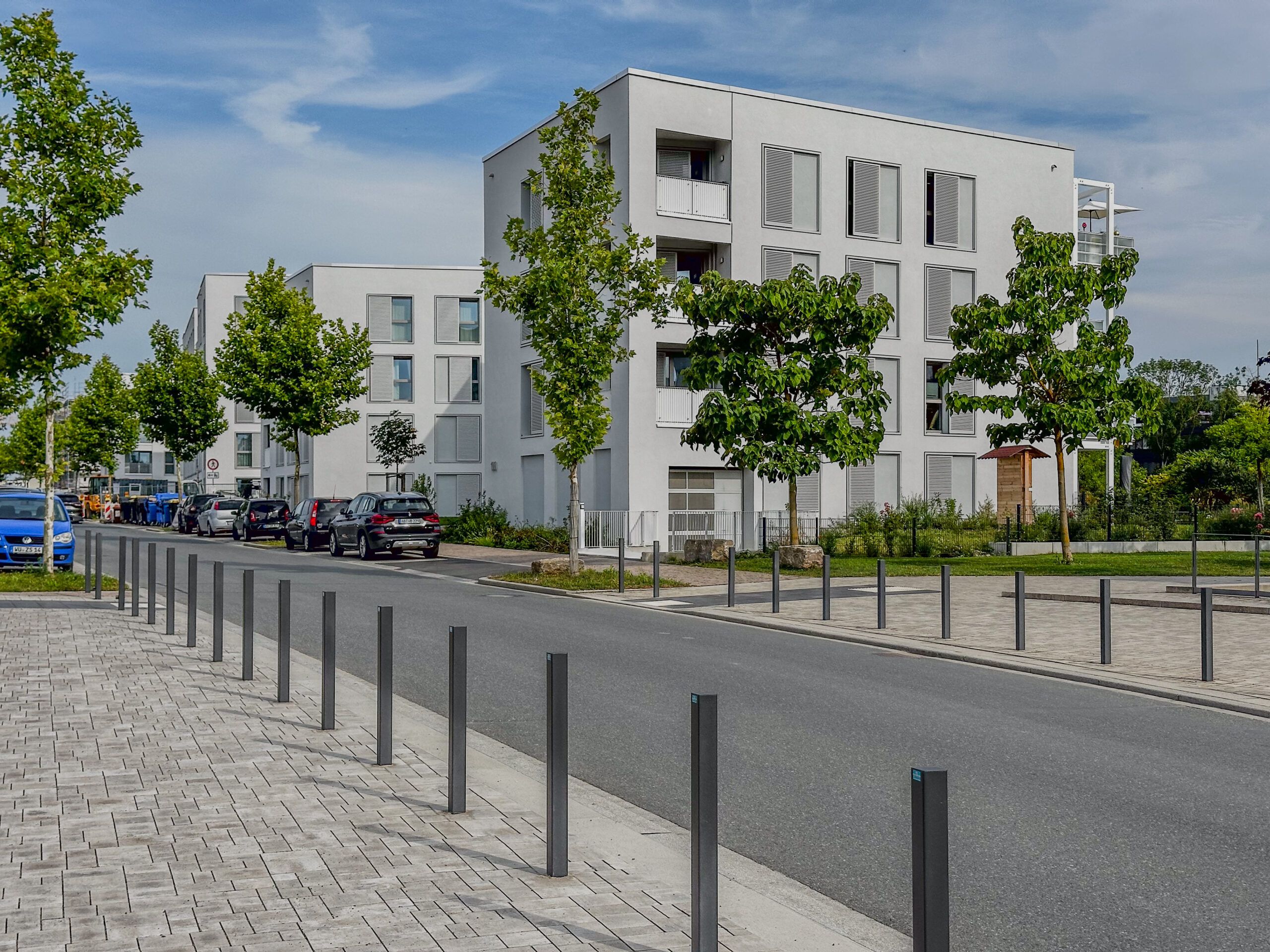 Eine Straße im neuen Stadtteil Hubland. Im Hintergrund sieht man Wohngebäude mit modernen Flachdächern.