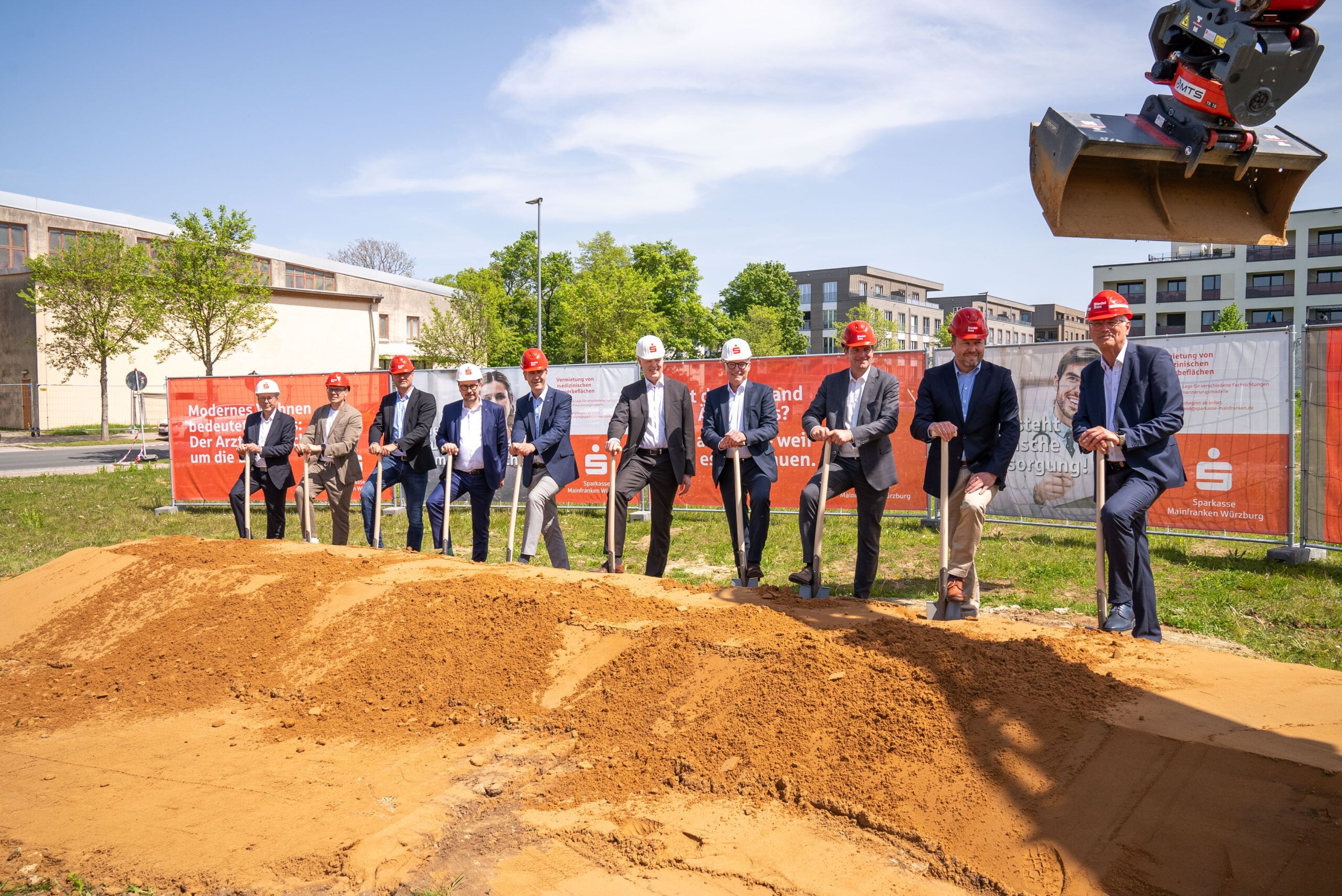 Spatenstich für das Ärztehaus am Hubland mit den Vorständen der Sparkasse. Die Männer haben Späten in der Hand. Im Vordergrund die erste ausgehobene Grube. Im Hintergrund der Bauzaun.