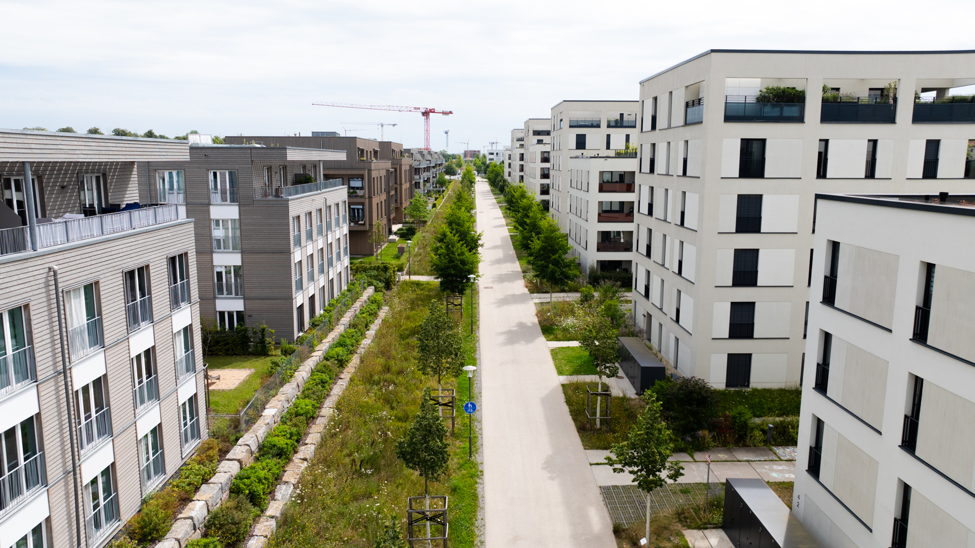 Drohnenaufnahme eines Fußwegs entlang im neuen Stadtteil Hubland. Rechts und links befinden sich Wohnhäuser. Der Weg ist an den Seiten begrünt